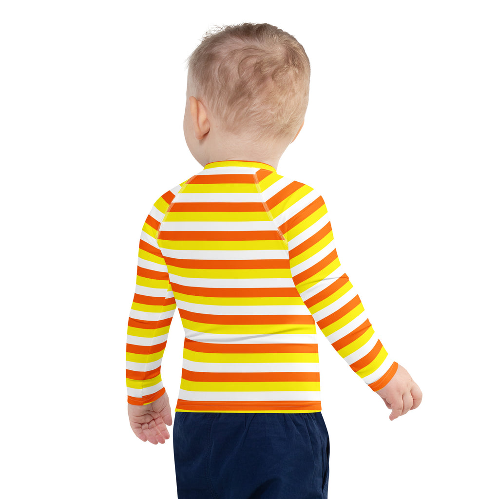 A child wearing a kids candy corn stripes halloween long sleeve rash guard in bright yellow orange and white with UPF 50+