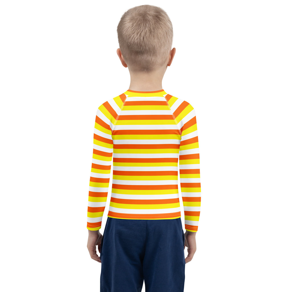 A child wearing a kids candy corn stripes halloween long sleeve rash guard swim shirt with upf 50 plus in orange yellow and white