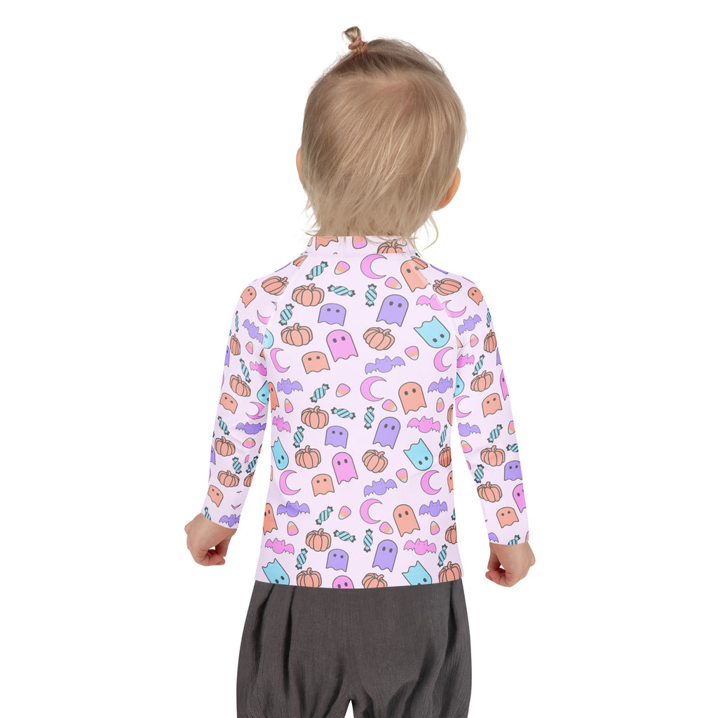 A child wearing a light pink girls halloween pattern long sleeve rash guard swim shirt with upf 50+ and colorful ghosts and pumpkins