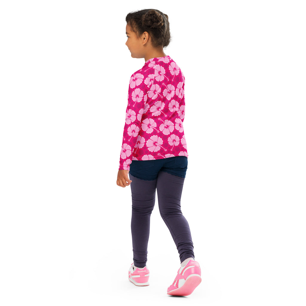 A vibrant pink girls tropical hibiscus long sleeve rash guard swim shirt with upf 50 plus worn by a child