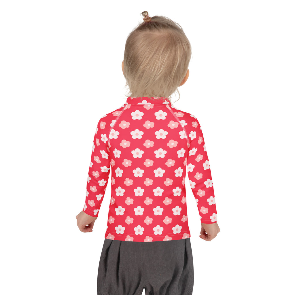 A girl wearing a red long sleeve rash guard with white and pink cherry blossom pattern and UPF 50 plus protection