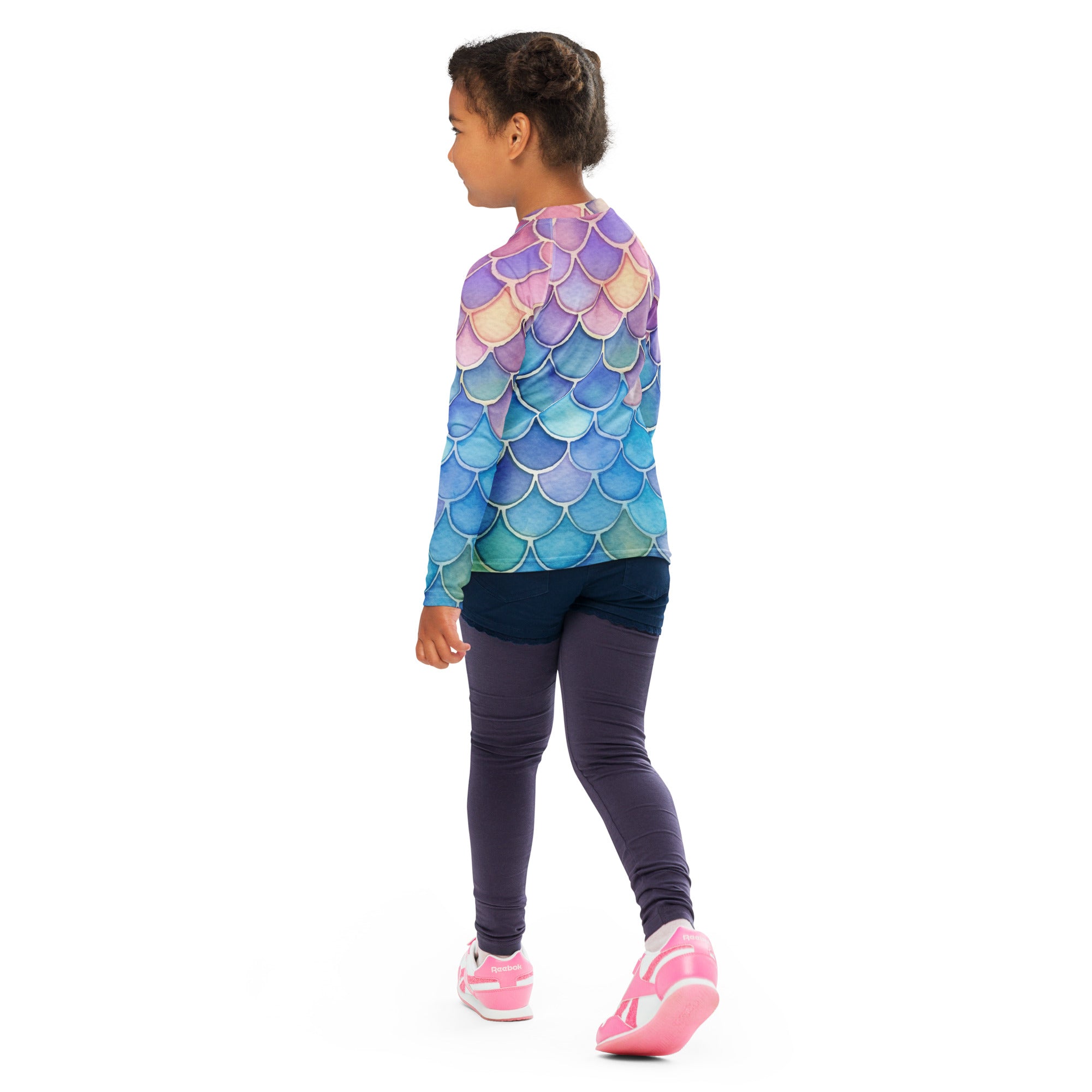 A child wearing a girls watercolor rainbow mermaid long sleeve rash guard swim shirt with iridescent purple pink blue scales and upf 50+