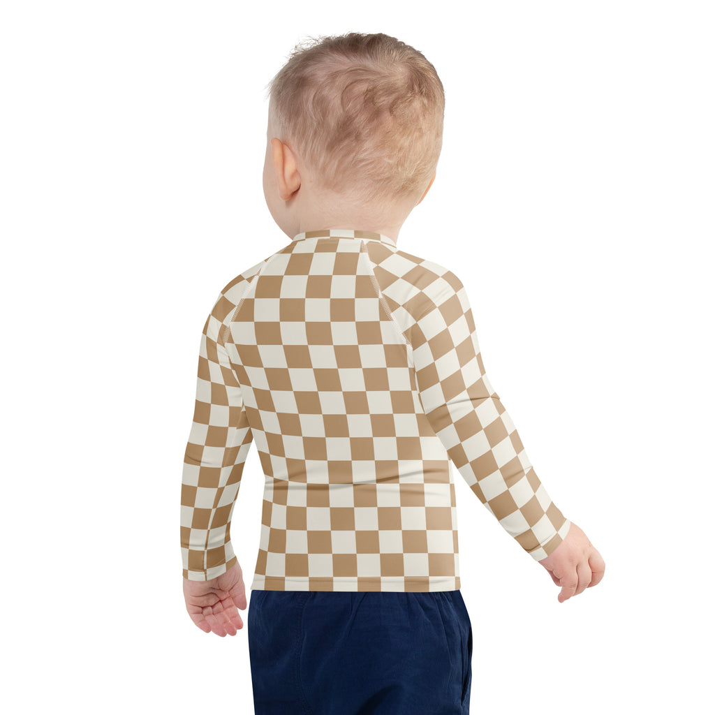 A child wearing a beige and cream checkered kids sand checkerboard long sleeve rash guard swim shirt with UPF 50+