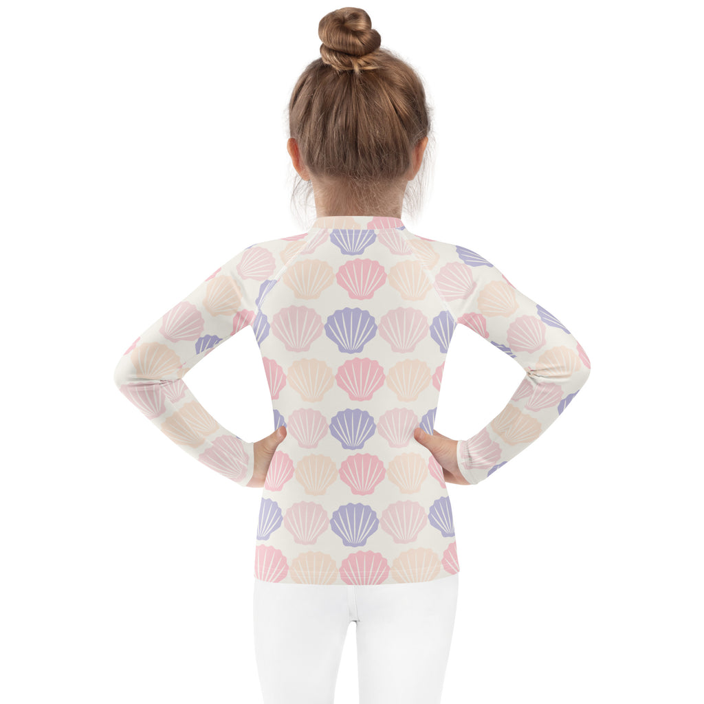 A girl wearing a kids seashell print long sleeve rash guard swim shirt with UPF 50 plus in pastel colors