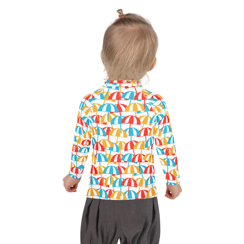 A child wearing a kids beach umbrella long sleeve rash guard swim shirt with vibrant red yellow and blue umbrellas