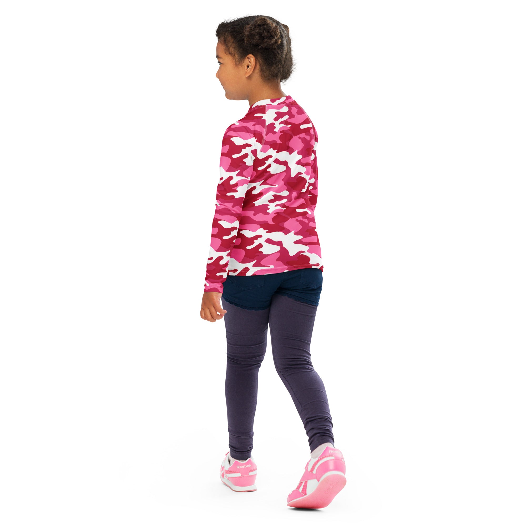 A girl wearing a pink and white camouflage long sleeve rash guard swim shirt with upf 50 plus and dark leggings