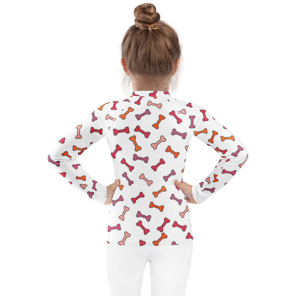 White kids long sleeve rash guard swim shirt with playful pink orange and red bone pattern and upf 50+ protection