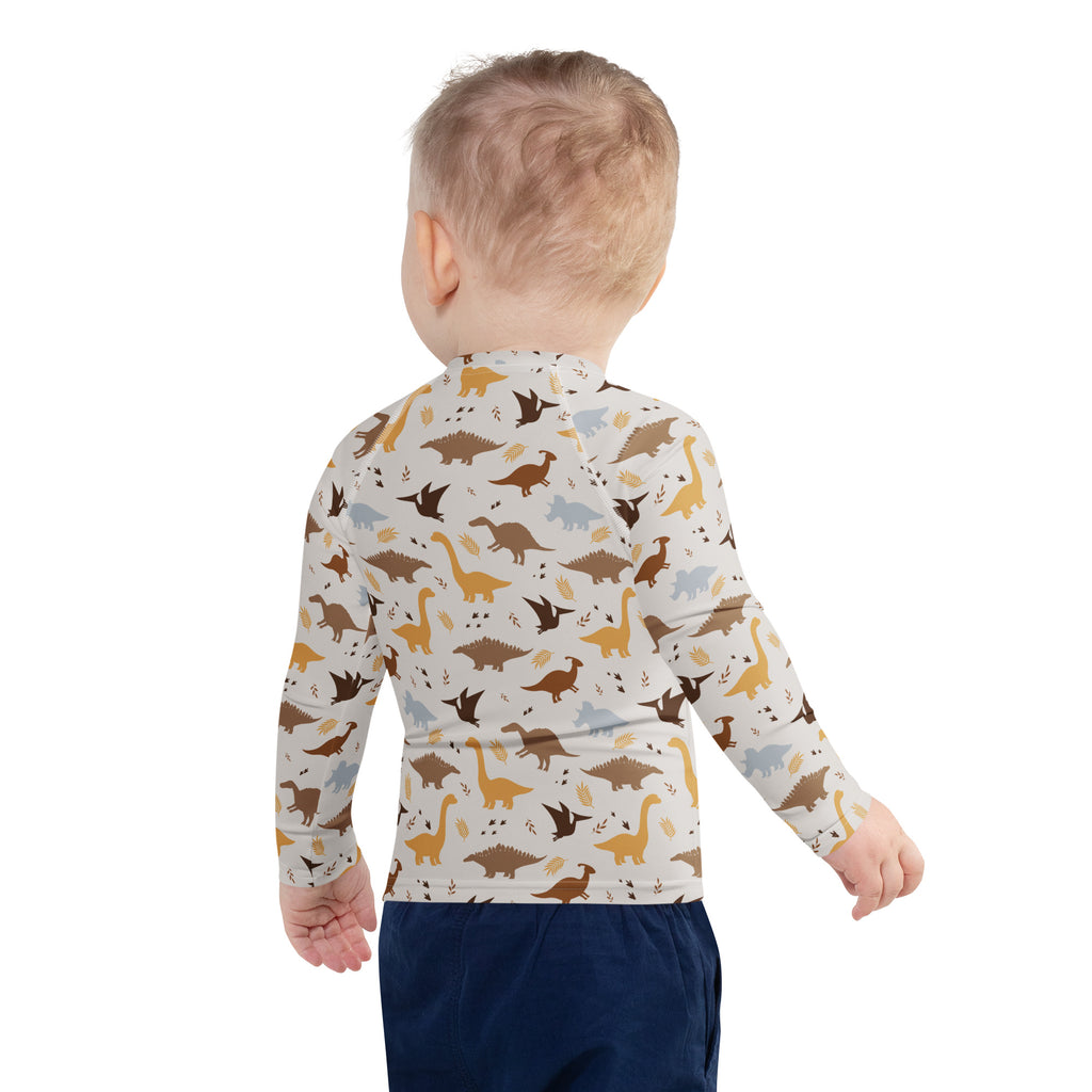 A child wearing a cream kids dinosaur long sleeve rash guard swim shirt with UPF 50 and playful dinosaur patterns
