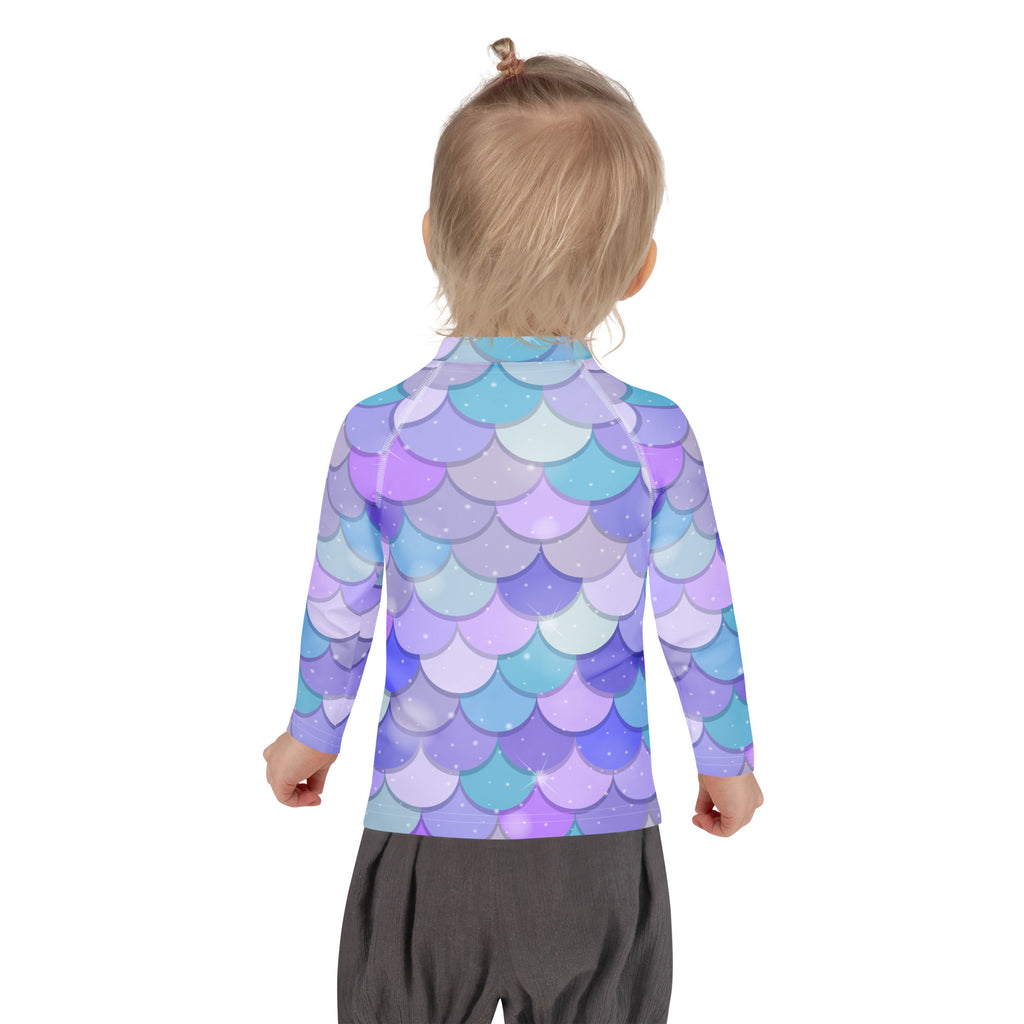 A girl wearing a purple mermaid scales long sleeve rash guard swim shirt with UPF 50 plus and glittery accents