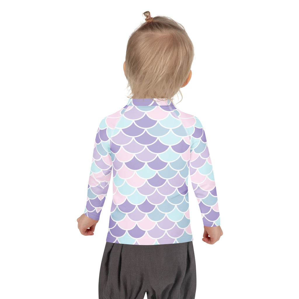 A child wearing a girls mermaid scale long sleeve rash guard swim shirt with upf 50 plus in pastel lavender blue and pink