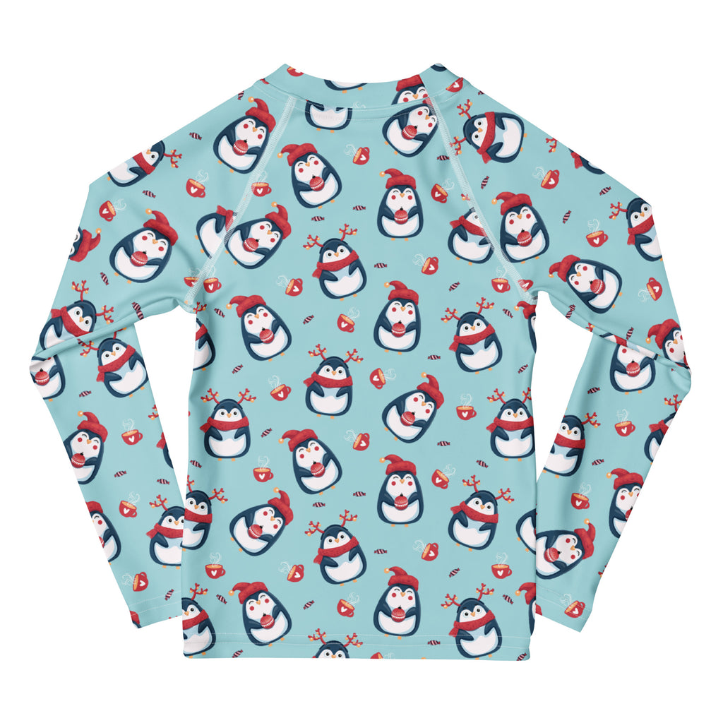 A light blue kids long sleeve rash guard swim shirt with UPF 50+ featuring cartoon penguins red hats scarves and reindeer antlers