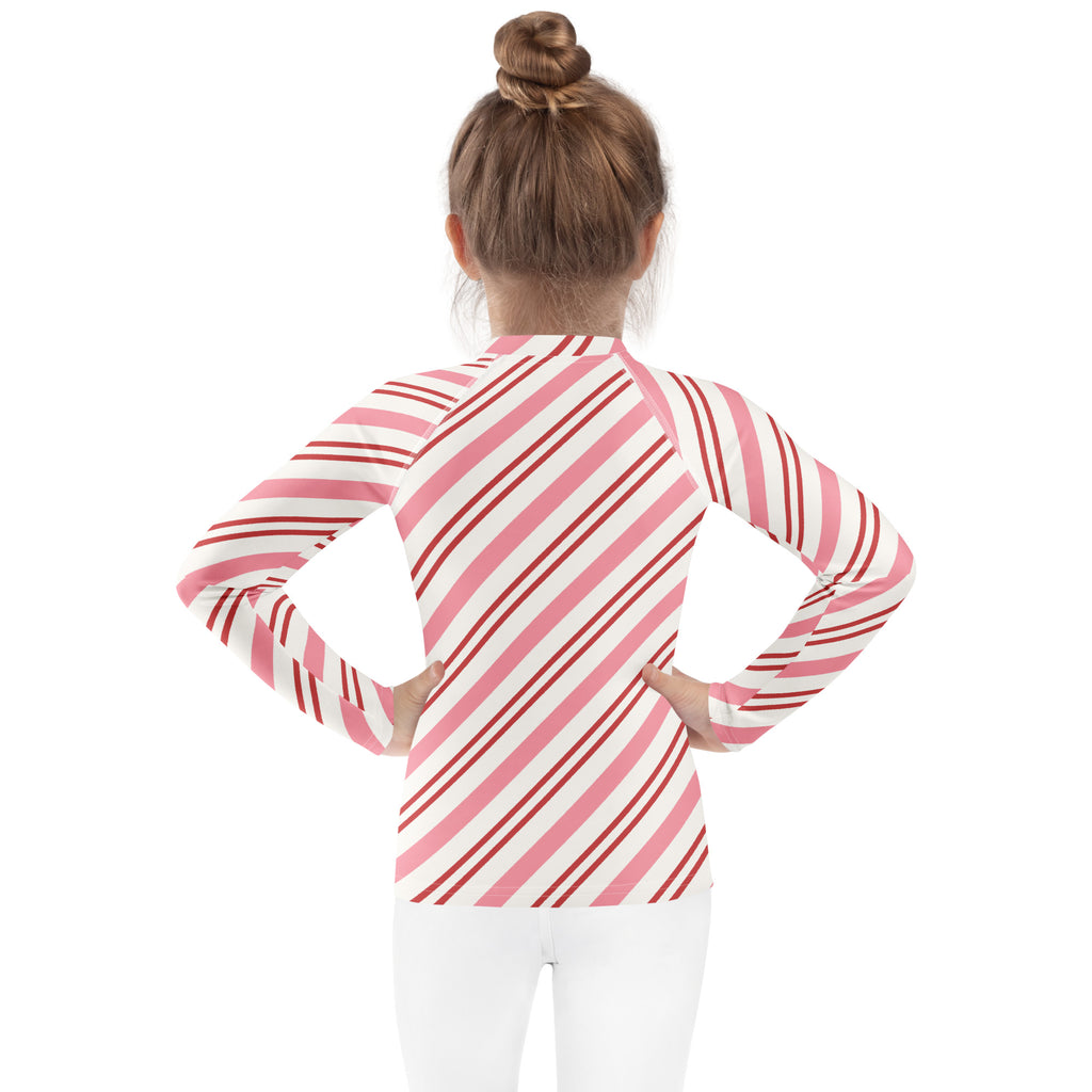A girl wearing a kids pink peppermint stripe long sleeve rash guard swim shirt with upf 50+ and red accents