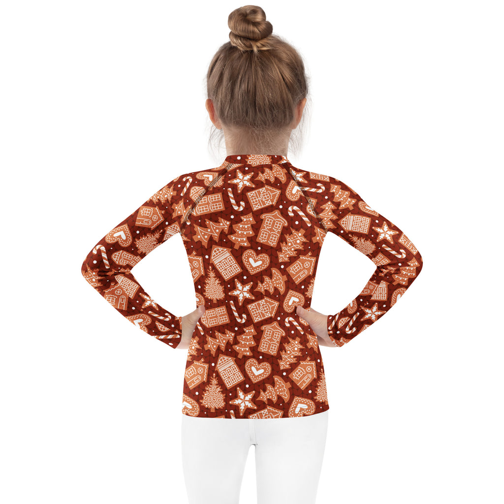 A girl wearing a kids red gingerbread christmas long sleeve rash guard swim shirt with upf 50 plus and candy cane pattern