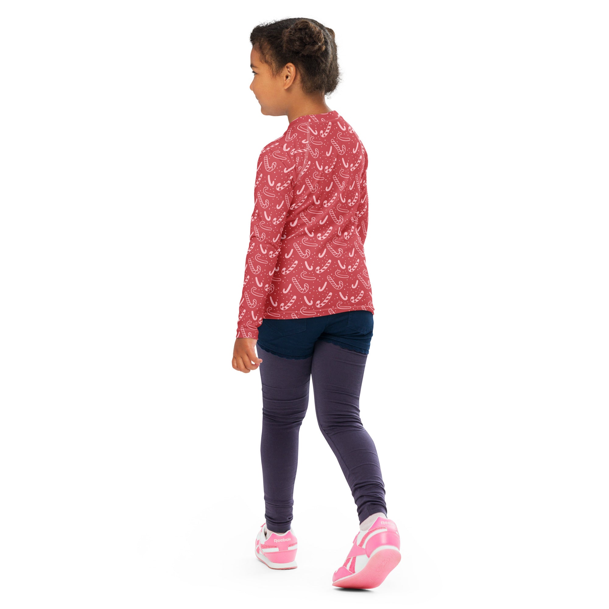 A child wearing a kids red candy cane christmas long sleeve rash guard swim shirt with UPF 50 plus and dark leggings