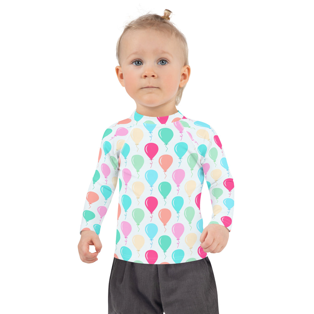 A child wearing a white kids birthday balloons long sleeve rash guard swim shirt with colorful pastel balloon print and UPF 50+