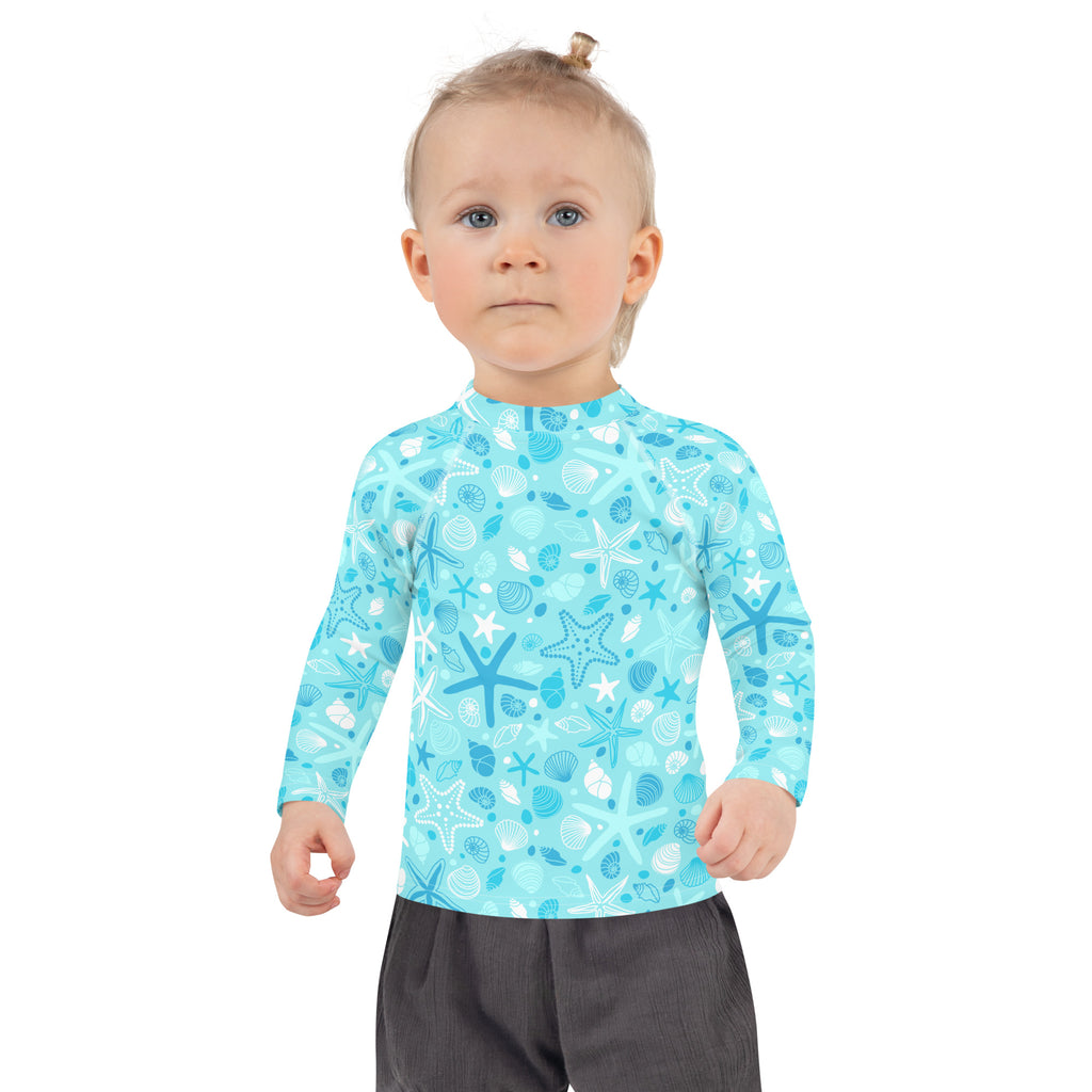 A child wearing a light blue kids starfish and seashell long sleeve rash guard with upf 50 plus for sun protection