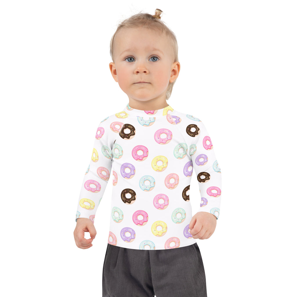 A child wearing a white kids colorful donuts long sleeve rash guard swim shirt with upf 50 and pastel donut prints