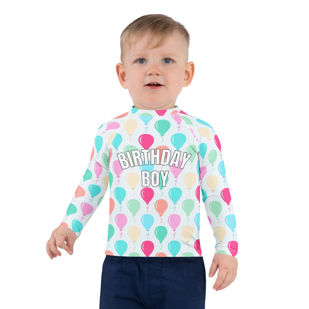 A child wearing a white long-sleeved birthday boy colorful balloons rash guard swim shirt with UPF 50+ protection
