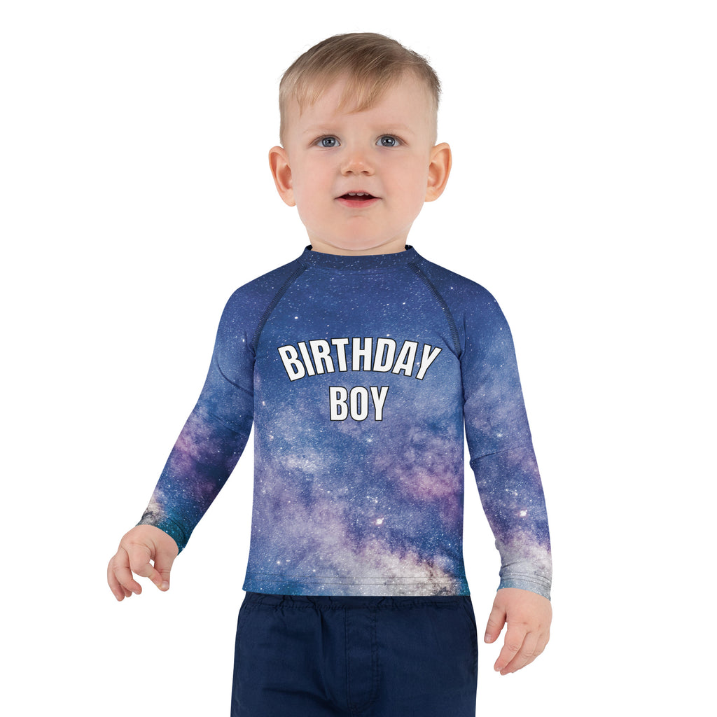 A child wearing a birthday boy realistic galaxy long sleeve rash guard swim shirt with upf 50 plus in blue and purple