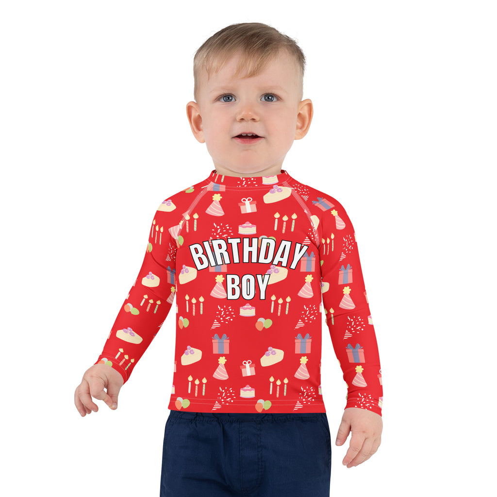 Toddler wearing a red 'Birthday Boy' shirt with birthday patterns on a white background