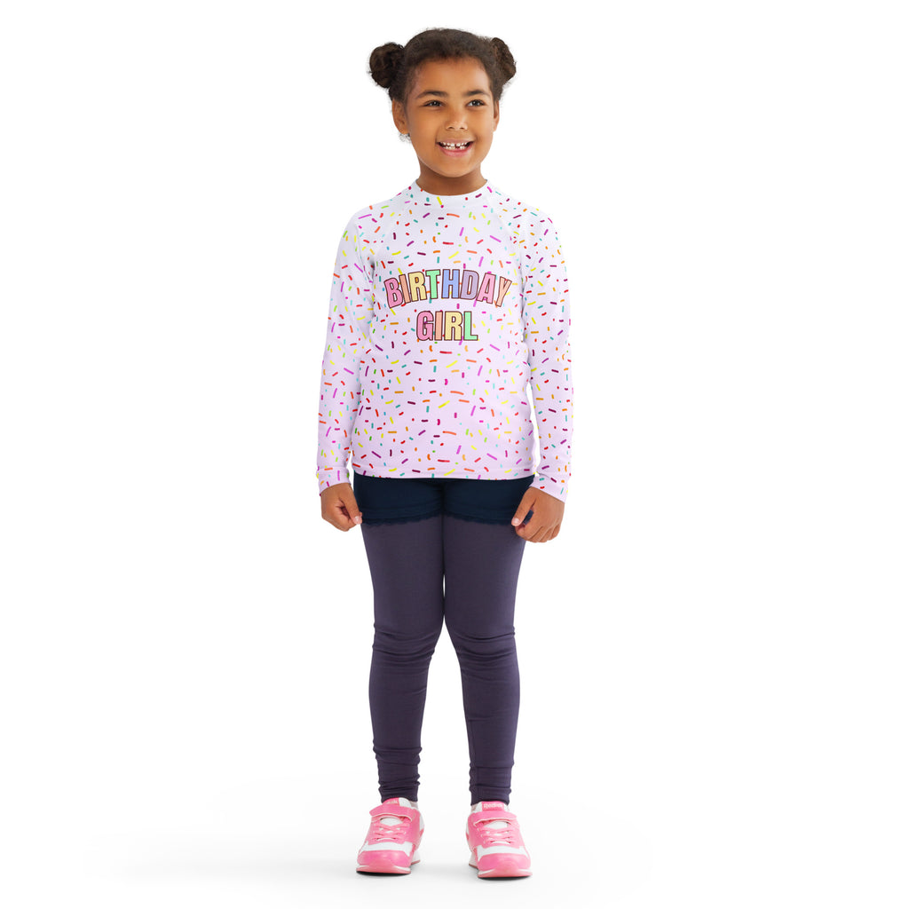 A child’s light pink long sleeve rash guard swim shirt with birthday girl graphic colorful sprinkles and upf 50+ protection