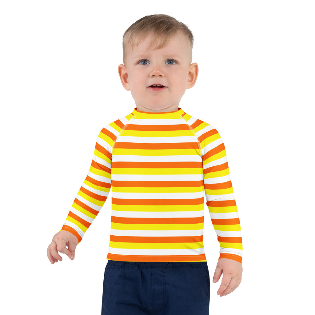 A child wearing a kids candy corn stripes halloween long sleeve rash guard swim shirt in bright yellow orange white
