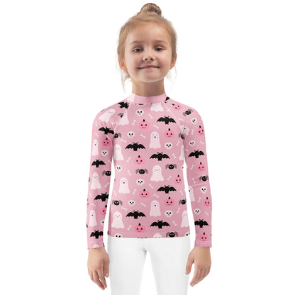 Girl wearing a pink Halloween-themed rash guard shirt with ghosts, bats, and pumpkins on a white background.