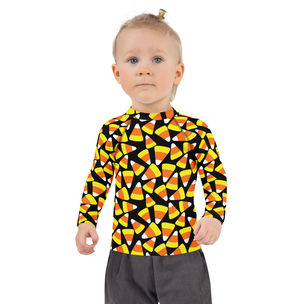 A child wearing a black kids candy corn halloween long sleeve rash guard swim shirt with upf 50+ and vibrant candy corn pattern