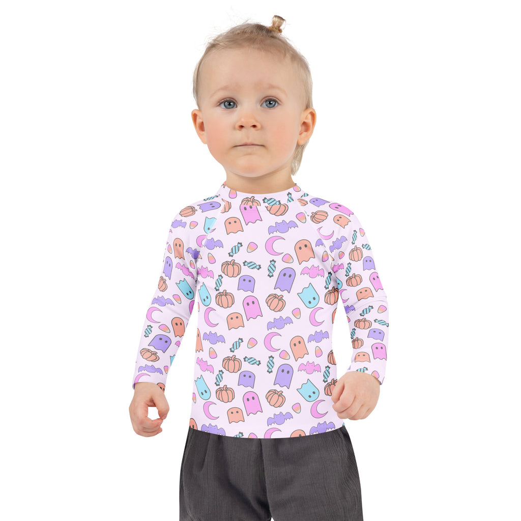 A girl wearing a white long sleeve halloween rash guard swim shirt with pastel ghosts pumpkins bats and UPF 50+ protection