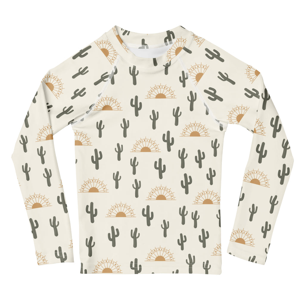 Cream-colored kids long sleeve rash guard with black cacti and tan sunbursts featuring UPF 50 plus sun protection
