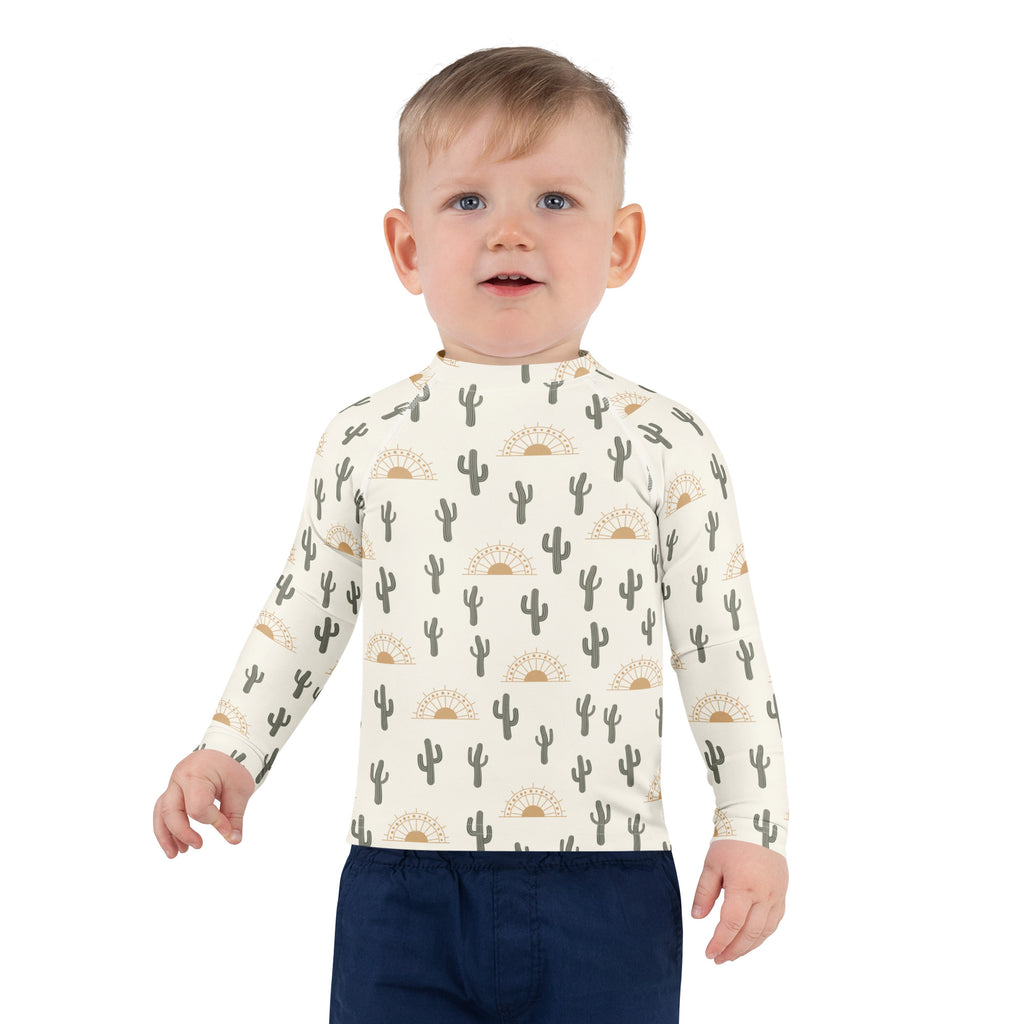 A child wearing a cream kids cactus desert sunrise long sleeve rash guard swim shirt with UPF 50+ and black cactus pattern