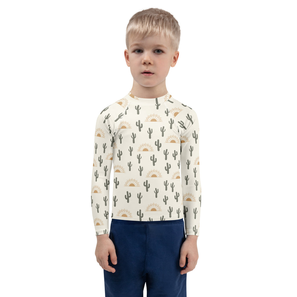 A child wearing a cream kids cactus desert sunrise long sleeve rash guard swim shirt with upf 50 and cactus print