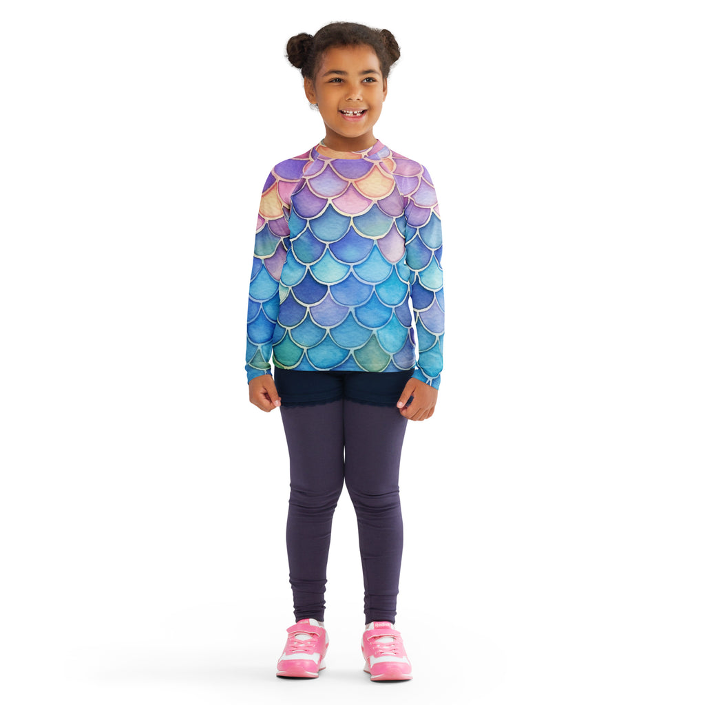 A child wearing a girls watercolor rainbow mermaid long sleeve rash guard swim shirt with upf 50+ in purple blue and teal