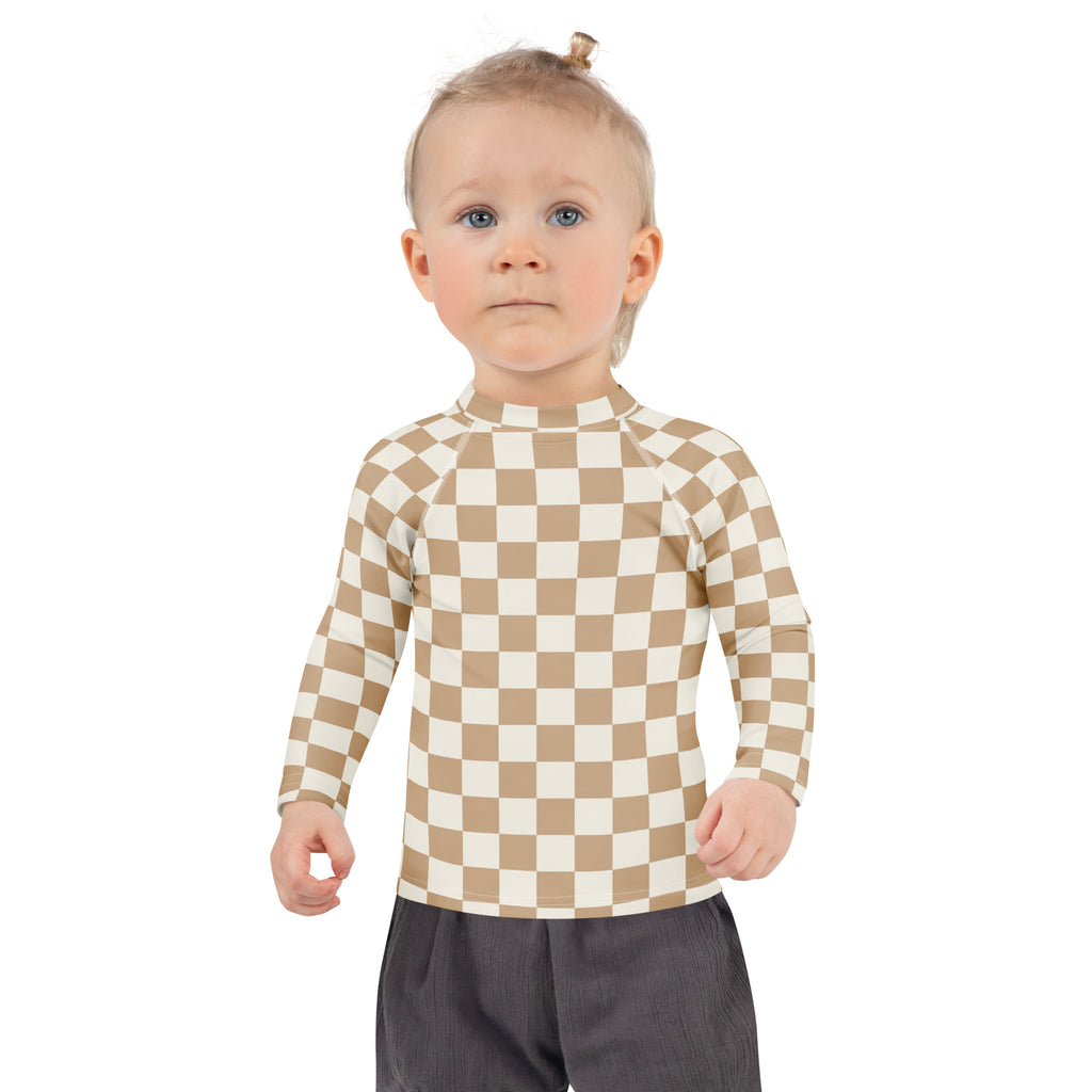 A child wearing a beige and cream checkered kids sand checkerboard long sleeve rash guard swim shirt with UPF 50+