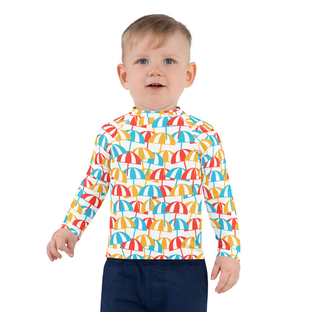 A child wearing a white kids beach umbrella long sleeve rash guard with colorful red blue and yellow umbrella patterns and UPF 50+