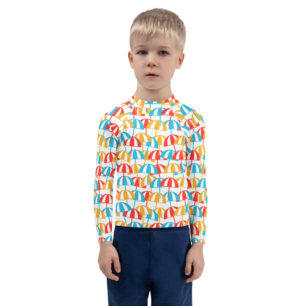 A child wearing a kids beach umbrella long sleeve rash guard with vibrant red yellow and blue umbrella pattern and UPF 50+