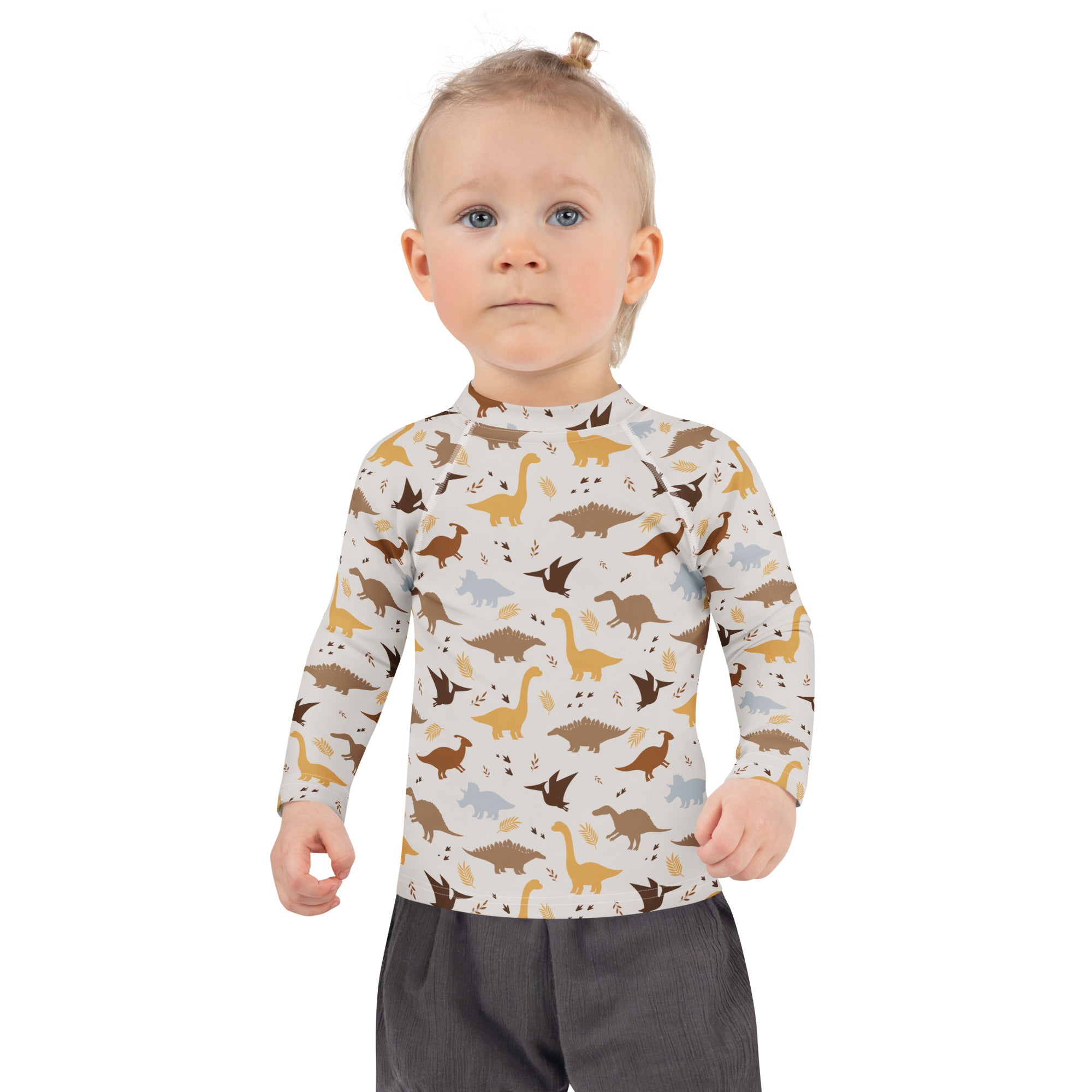 A child wearing a cream longsleeve kids dinosaur rash guard swim shirt with brown gold dinosaur print and UPF 50 plus protection