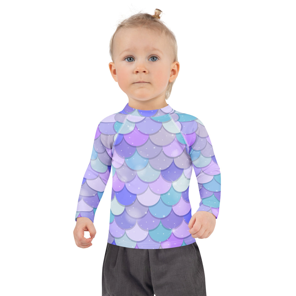 A girl wearing a purple and blue mermaid scales long sleeve rash guard swim shirt with UPF 50 plus and glitter accents