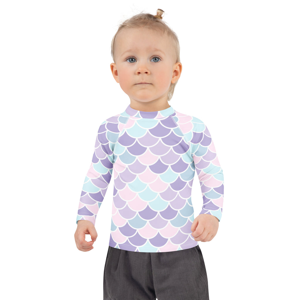 A child wearing a girls mermaid scale long sleeve rash guard swim shirt with upf 50 plus in pastel lavender blue and pink