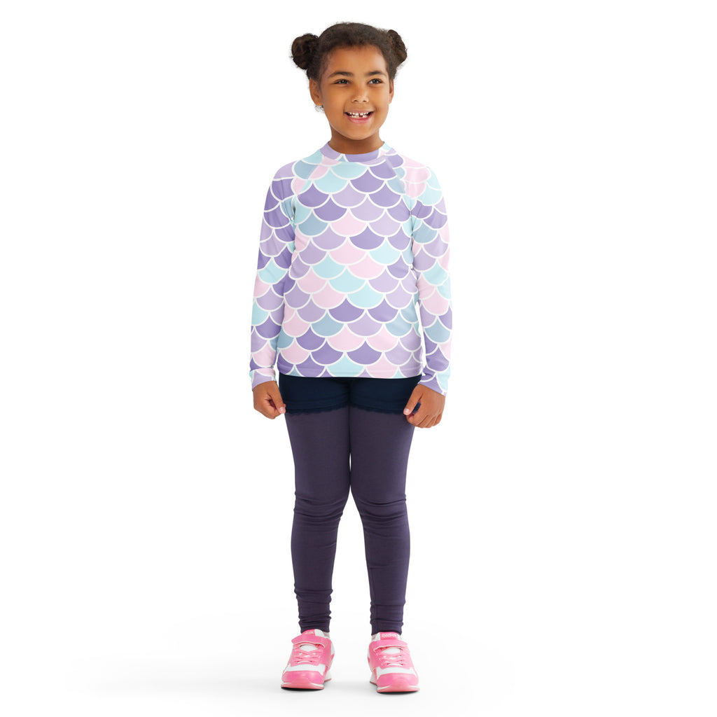A child wearing a girls mermaid scale long sleeve rash guard swim shirt with upf 50+ in pastel lavender blue pink
