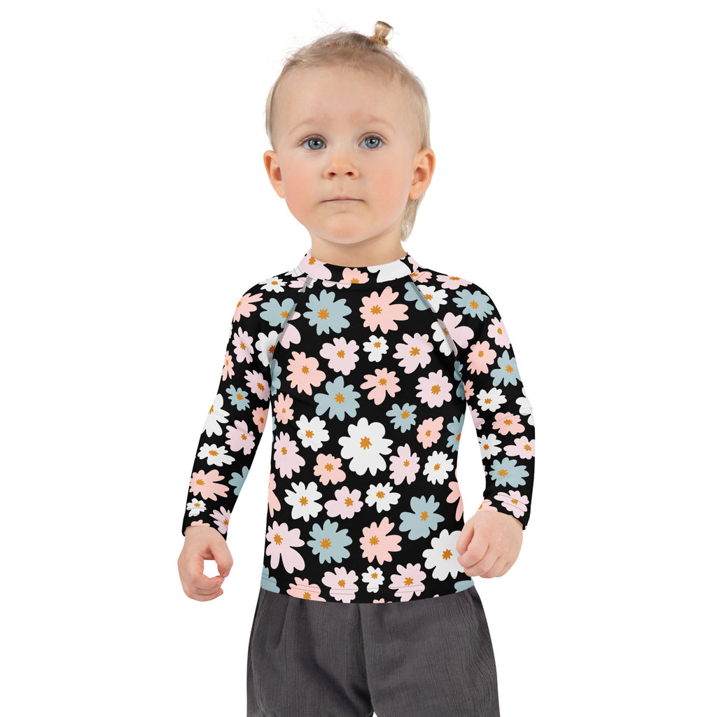 A girl wearing a black girls flower scale long sleeve rash guard swim shirt with pink white and blue daisies and UPF 50+