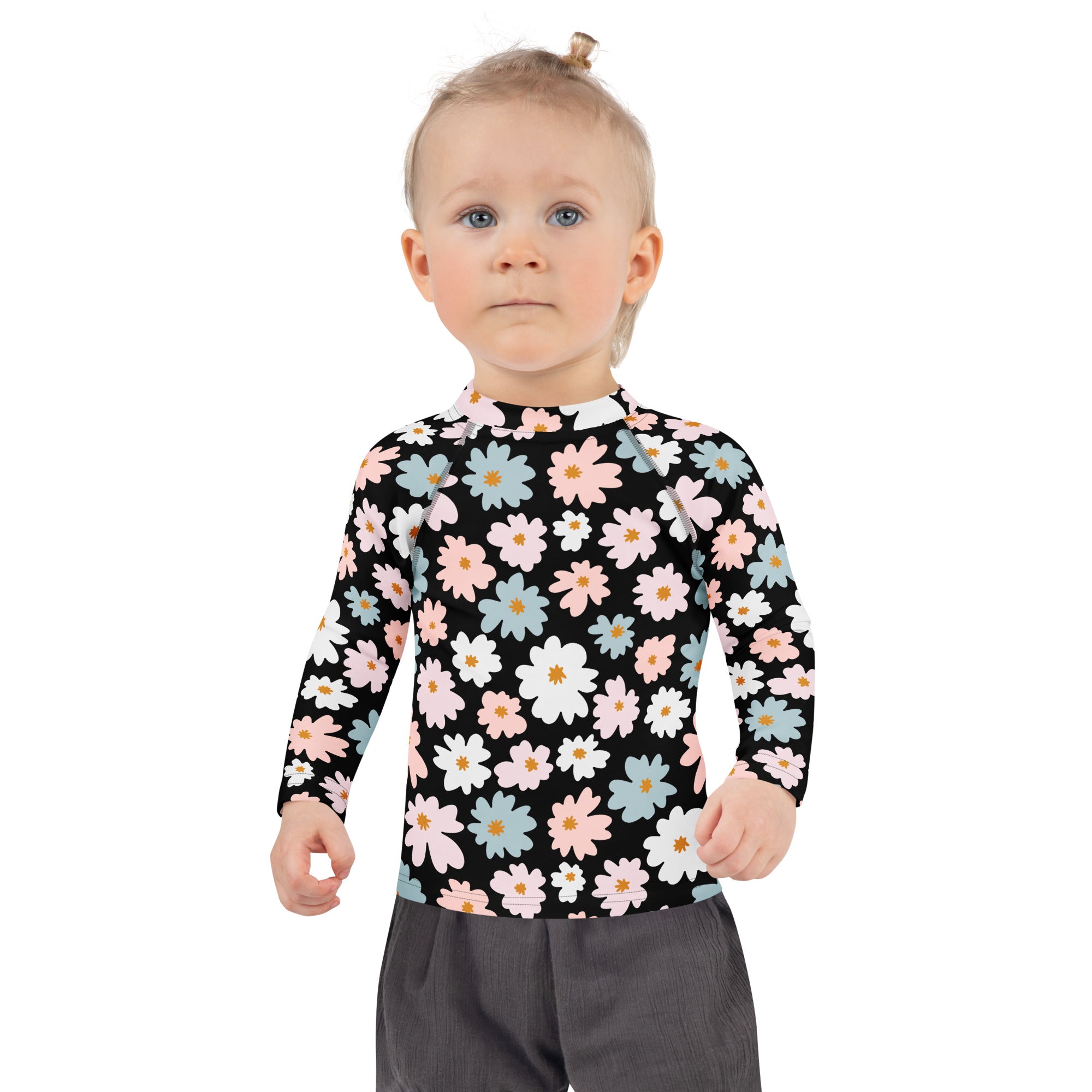 A girl wearing a black girls flower scale long sleeve rash guard swim shirt with pink white and blue daisies and UPF 50+