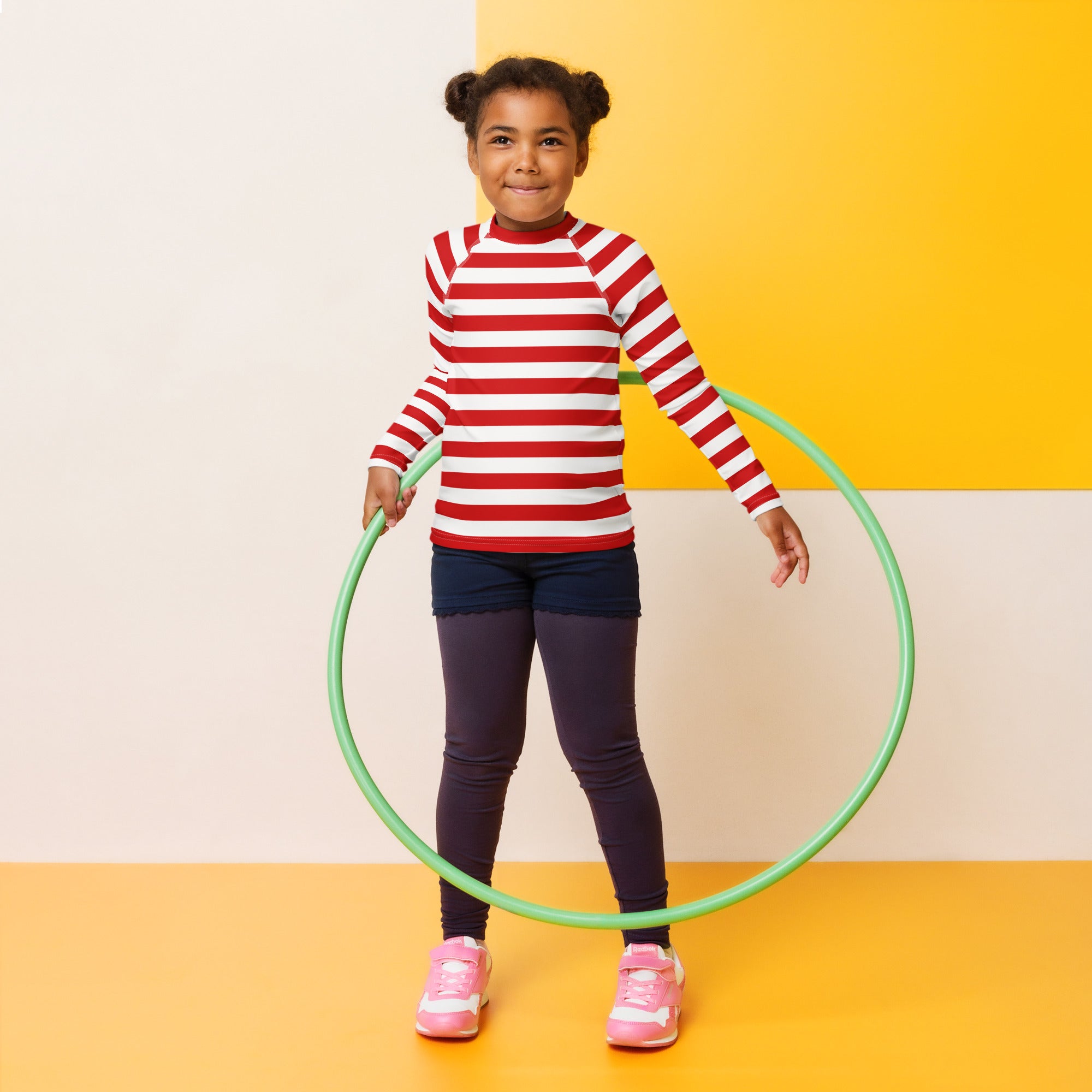 Green plastic hula hoop alongside kids red and white striped christmas long sleeve rash guard swim shirt with upf 50+