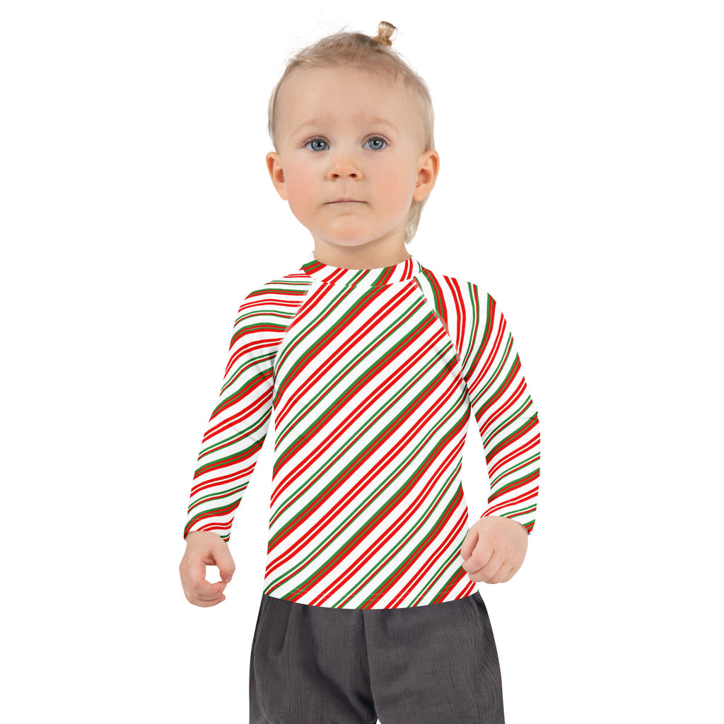 A child wearing a kids candy cane stripe christmas long sleeve rash guard with red green and white stripes and UPF 50+ protection