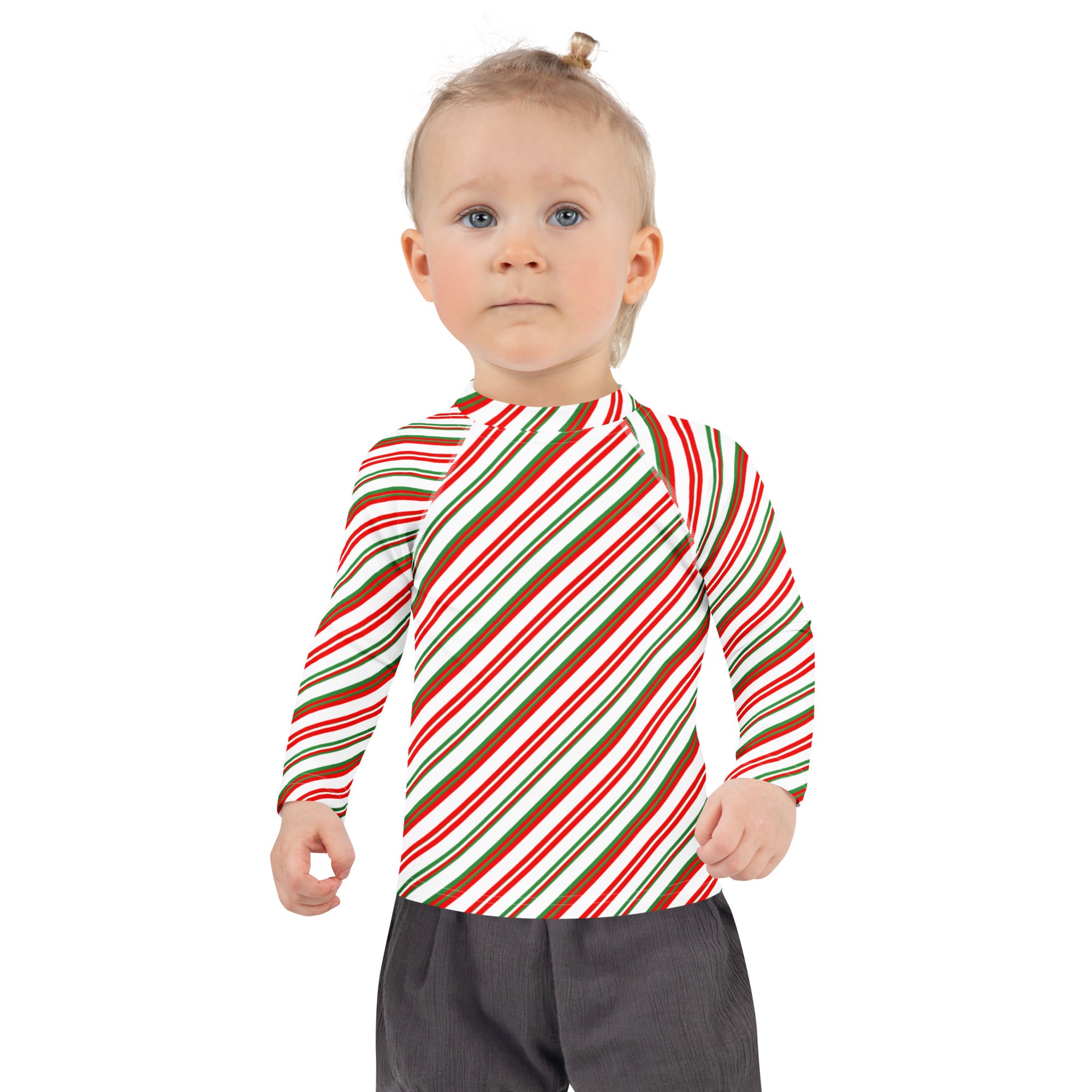 A child wearing a kids candy cane stripe christmas long sleeve rash guard with red green and white stripes and UPF 50+ protection