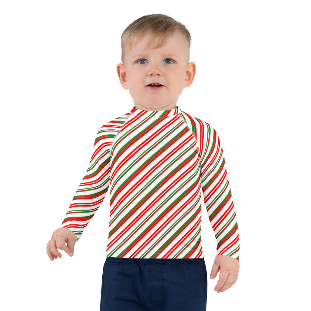 A child wearing a kids candy cane stripe christmas long sleeve rash guard with diagonal red green and white stripes and UPF 50+