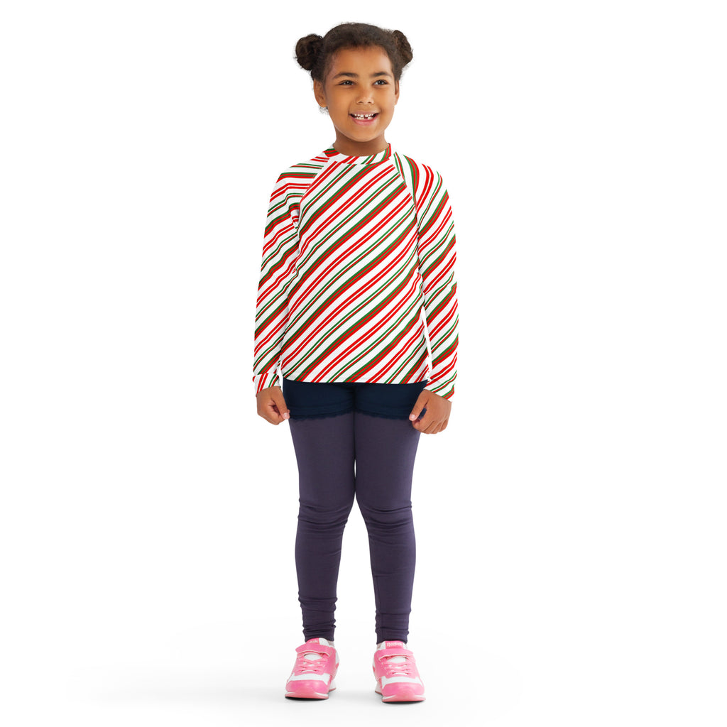 A child wearing a kids candy cane stripe christmas long sleeve rash guard swim shirt with upf 50 plus in red white and brown