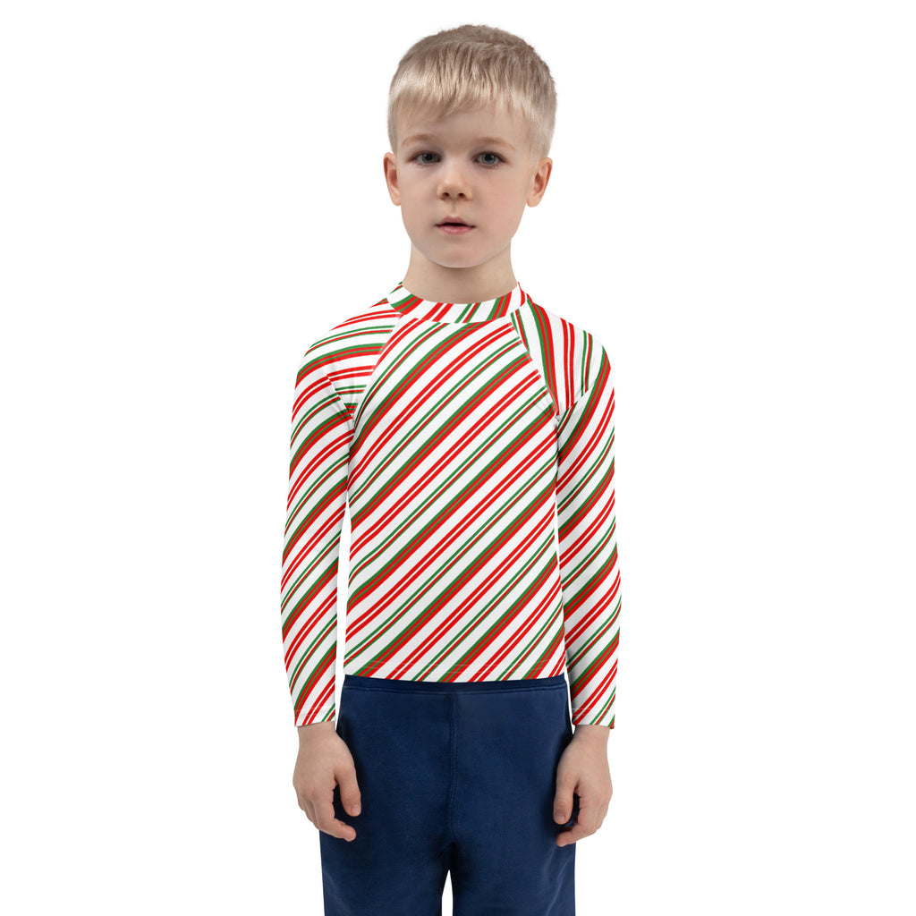 A child wearing a kids candy cane stripe christmas long sleeve rash guard swim shirt with upf 50 plus and diagonal red green and white stripes