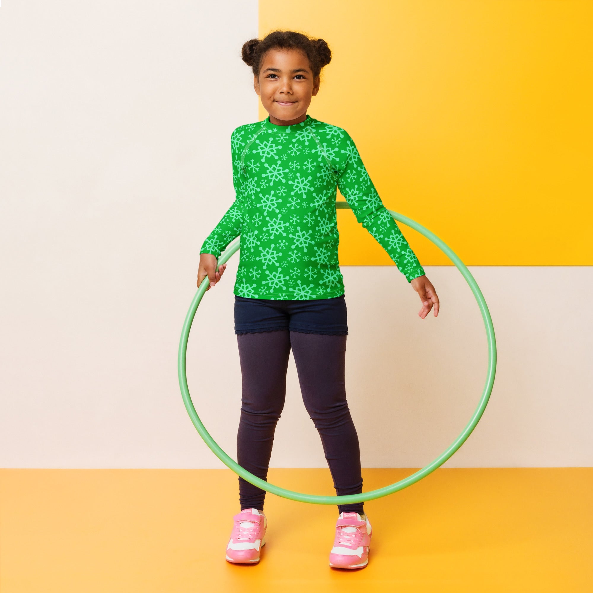 Green hula hoop with a smooth slightly glossy finish alongside a kids green snowflake christmas rash guard swim shirt with upf 50+