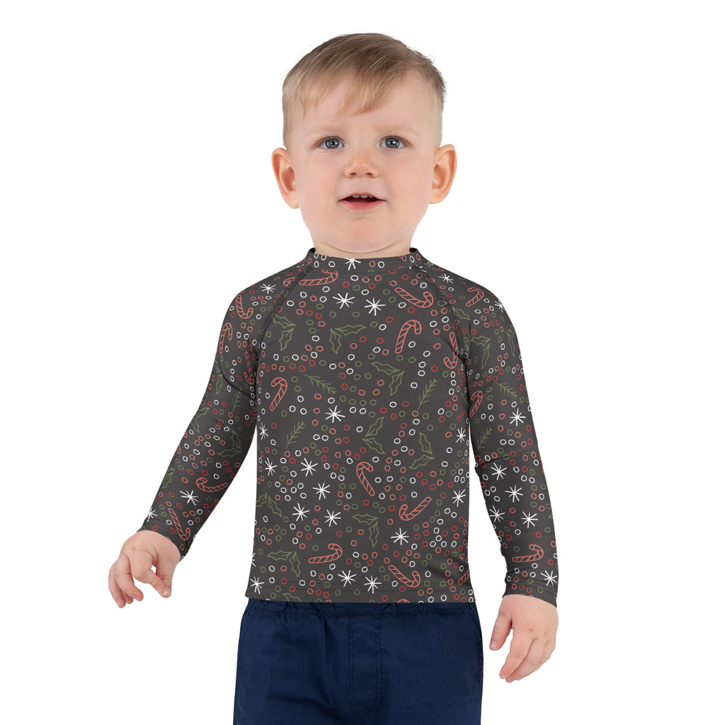 A child wearing a dark gray kids candy cane and holly christmas long sleeve rash guard with UPF 50+ protection